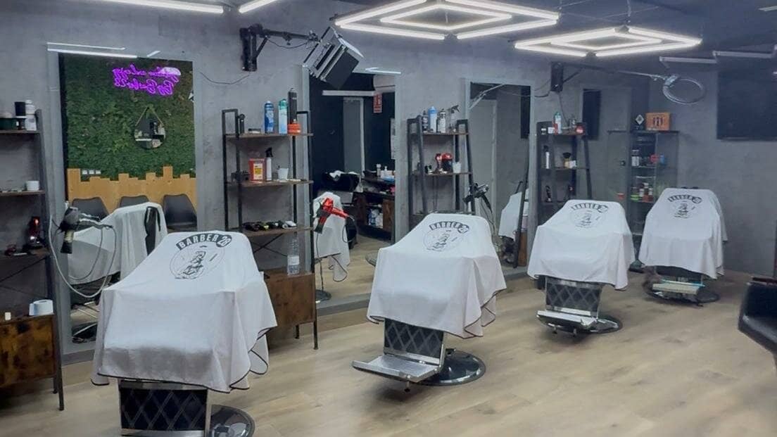 Inside the Churriana de la Vega shop: four barber chairs draped in white Barber28 capes facing the mirrors, under geometric ceiling lights