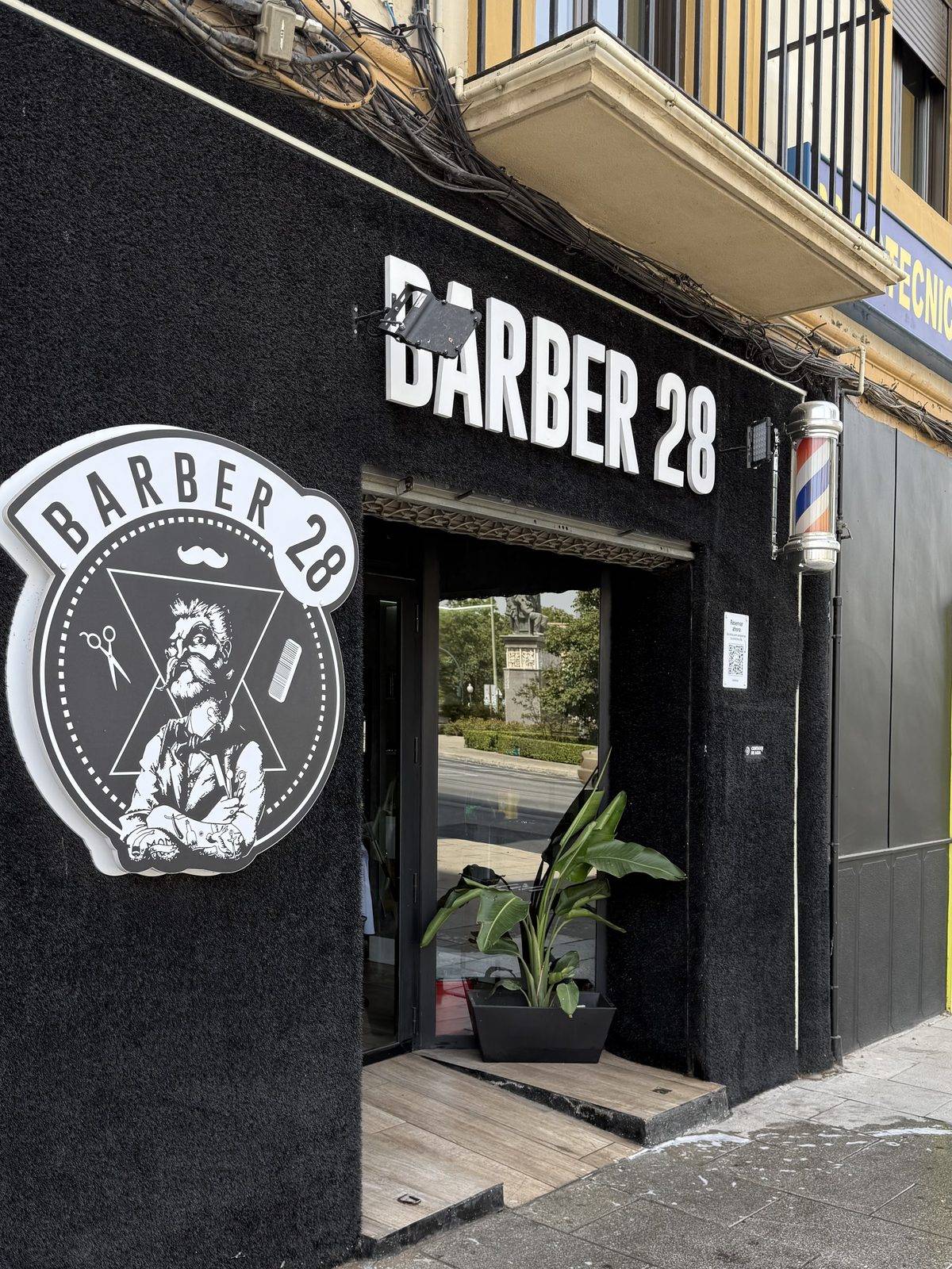 The Granada city centre shop from the street: BARBER 28 in white letters on a black wall, the shop's emblem and a barber pole by the door