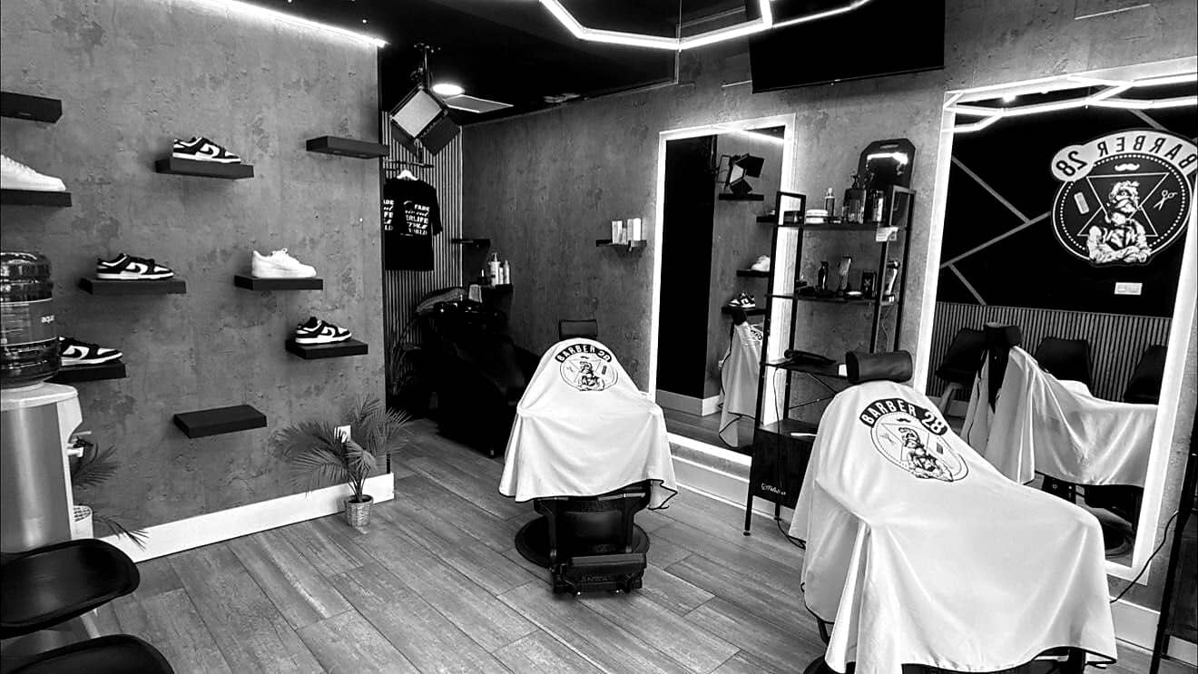 Interior de Barber28 Granada Centro: sillones con capas del logo y pared de hormigón