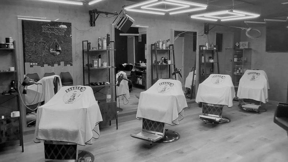 Interior de Barber28 Churriana de la Vega: fila de sillones con capas blancas bajo luces geométricas